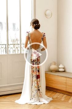 a woman standing in front of a window with her back turned to the camera and wearing a white dress