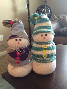 two knitted snowmen sitting next to each other on top of a wooden table