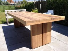 a wooden table sitting in the middle of a yard next to a white chair and some bushes