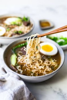 a bowl of ramen with chopsticks and an egg in the middle, on a marble table