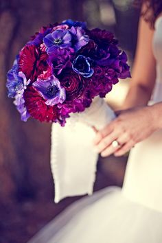 a bride holding a bouquet of purple and red flowers