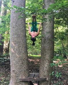 a person hanging upside down in the air between two trees with their hands on them