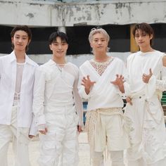 four young men standing next to each other in white outfits and holding their hands up