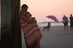 a woman wrapped in a towel hugging a man on the beach with people walking by