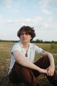 a woman sitting on the ground in a field with her hands crossed and looking at the camera