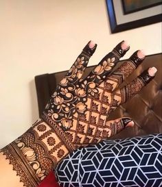 a woman's hands with henna tattoos on her arm and hand, sitting next to a couch