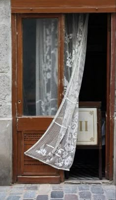 a woman walking past a window with a white lace curtain hanging from it's side