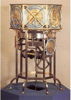 an antique clock with gears and dials on it's sides, sitting on top of a blue platform