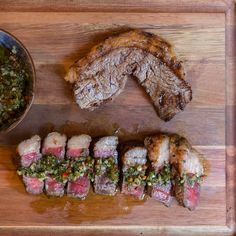 some meat and vegetables are sitting on a cutting board next to a bowl of sauce