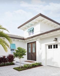 a white house with a brown door and palm tree in the front yard on a sunny day