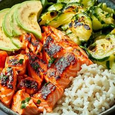 a bowl filled with salmon, rice and avocado on top of a table