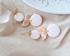 three white and gold earrings sitting on top of a table next to a plate with black speckles