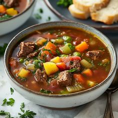 a bowl of soup with meat, vegetables and bread