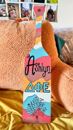 a wooden bottle shaped like a flower with the words ashlyn age on it sitting next to a teddy bear