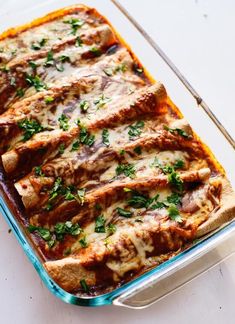 a casserole dish with meat, cheese and parsley in it on a white surface