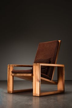 a wooden chair sitting on top of a cement floor next to a brown cushion and pillow