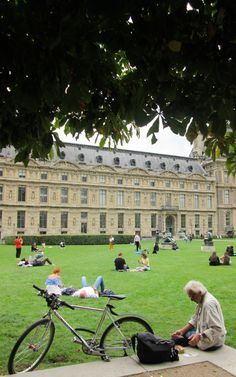 people sitting on the grass in front of a building with a bicycle parked next to it