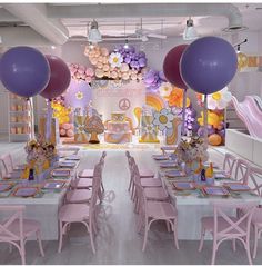 a room filled with lots of tables covered in purple and pink balloons next to white walls