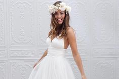 a woman wearing a white dress and flower headpiece standing in front of a wall