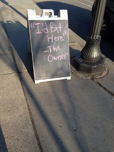 a chalkboard sign sitting on the sidewalk next to a street light and lamp post