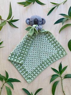 a green crocheted cloth with a teddy bear on it and leaves surrounding it