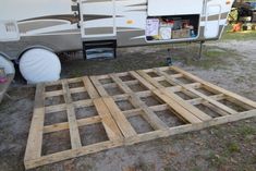 a camper trailer sitting in the grass next to a pile of wood planks