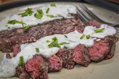 two steaks covered in white sauce and parsley on a plate with a fork