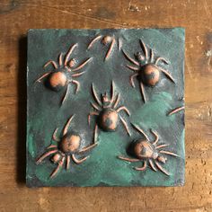 a tile with four spider on it sitting on top of a wooden table in front of a wall