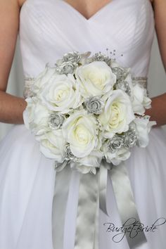 the bride's bouquet is made up of white roses and silver ribbon, which matches her dress