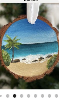 a christmas ornament hanging from a tree with a beach scene painted on it