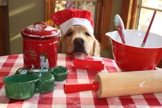 a dog wearing a santa hat sitting at a table with baking supplies and utensils