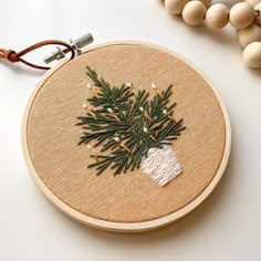 a cross stitch christmas tree ornament on a wooden hoop with bead and wood beads