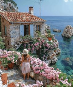 a woman in a hat is looking out at the water and flowers on the shore