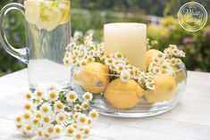 lemons and daisies in a glass bowl with a candle on a table outside