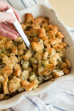 a person holding a fork in a casserole dish with bread and vegetables on it