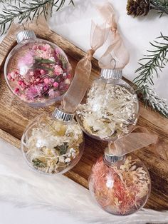 three glass ornaments on a wooden tray with pine cones and flowers in the middle one is filled with confetti