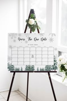 a calendar on a easel in front of a window with flowers and greenery