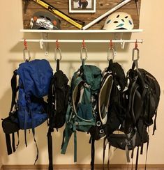 several backpacks and helmets hanging from hooks on a wall with a helmet mounted above them