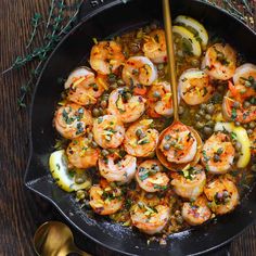 a skillet filled with cooked shrimp and lemon wedges, garnished with herbs