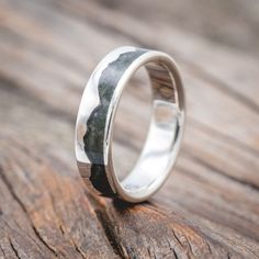 a silver ring with black and white marble inlays on the outside, sitting on a wooden surface