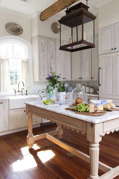 a large kitchen island in the middle of a wooden floored room with white cabinets