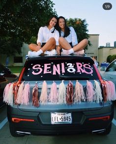 two women sitting on the back of a car decorated with pink and white tassels