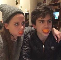 two people with orange peels in their mouths, one is looking at the camera