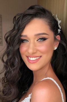 a woman with long dark hair wearing a white dress and flower in her hair, smiling at the camera