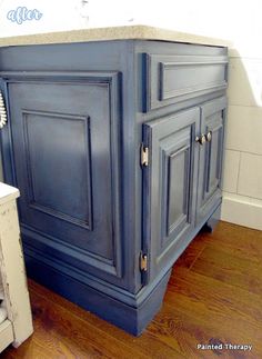 a bathroom vanity with blue painted cabinets and wood flooring in front of a window