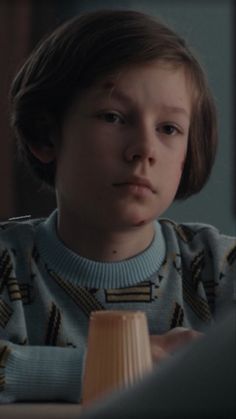 a young boy sitting at a table with a wooden block in front of him