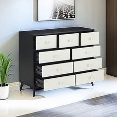 a black and white dresser with drawers next to a potted plant on the floor