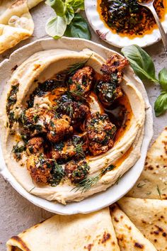 hummus with roasted cauliflower and herbs in a white bowl surrounded by pita bread