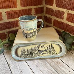 two coffee mugs sitting on top of each other next to a brick wall and plant