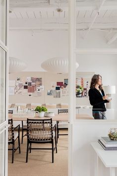 a woman standing in an office looking out the window at her work space and desks